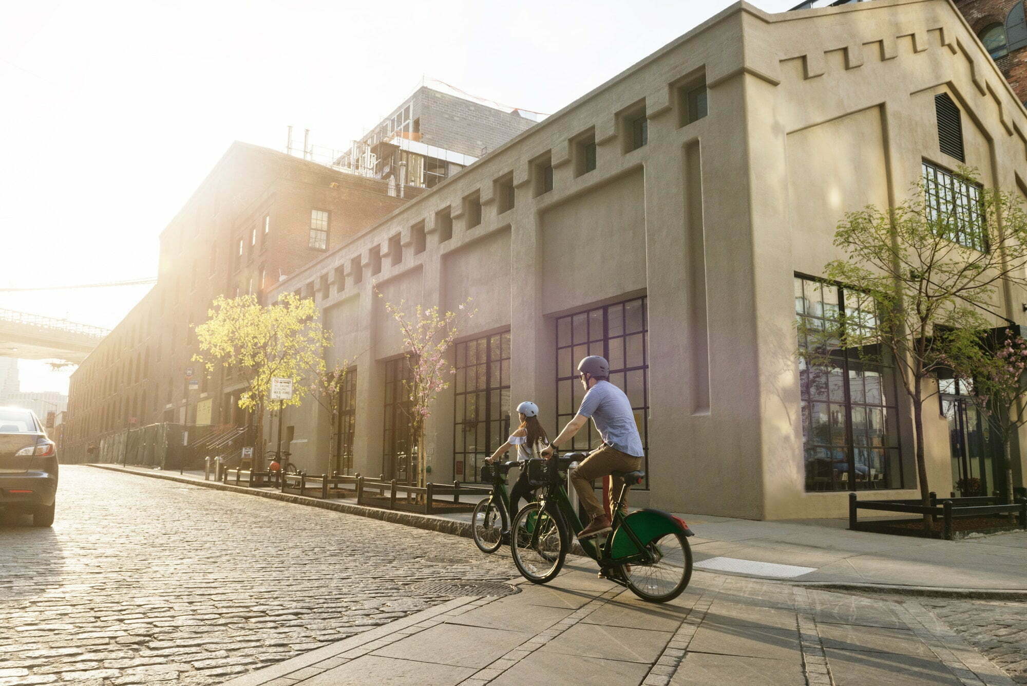 Couple Cycling On Road By Building In City Against Sky